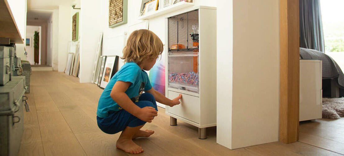 Et lite barn som bruker pressen til å åpne oppbevaringsrommet til Qute hamster og ørkenrotte buret.