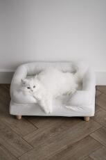 En hvit katt som nyter komforten til den hvite støttesengen sin