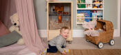 Baby på gulvet i et lekerom med en Qute hamster og ørkenrotte bur.