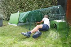 En person som demonstrerer hvordan man rengjør en kaninløp koblet til en grønn hytte