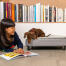 Hund sitter på Omlet Topology hundeseng med vattert topp og svarte skinneføtter undersøker jentebok