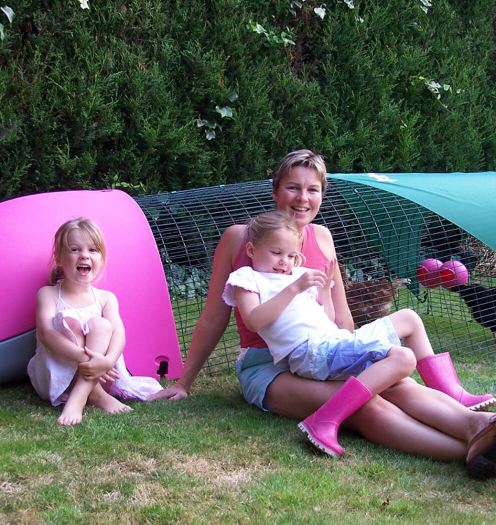En familie som sitter ved siden av et rosa Eglu hønsehus.